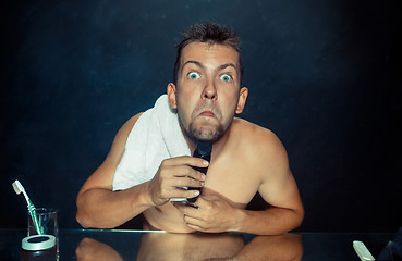 Image showing young man in bedroom sitting in front of the mirror scratching his beard