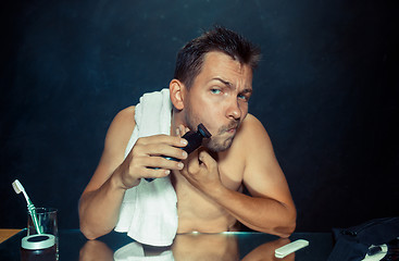 Image showing young man in bedroom sitting in front of the mirror scratching his beard