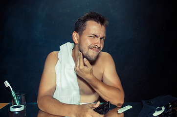 Image showing young man in bedroom sitting in front of the mirror scratching his beard