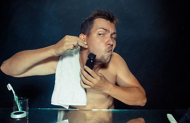 Image showing young man in bedroom sitting in front of the mirror scratching his beard