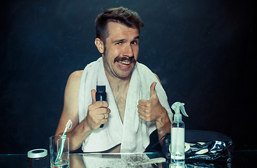 Image showing young man in bedroom sitting in front of the mirror scratching his beard