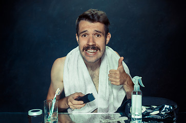 Image showing young man in bedroom sitting in front of the mirror scratching his beard