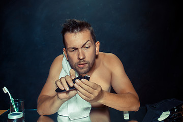 Image showing young man in bedroom sitting in front of the mirror scratching his beard