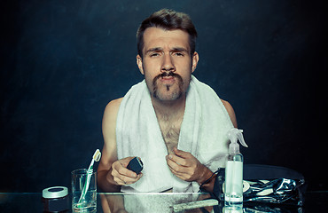 Image showing young man in bedroom sitting in front of the mirror scratching his beard