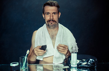 Image showing young man in bedroom sitting in front of the mirror scratching his beard