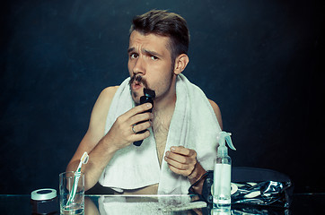 Image showing young man in bedroom sitting in front of the mirror scratching his beard