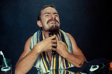 Image showing young man in bedroom sitting in front of the mirror scratching his beard