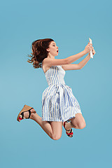 Image showing Image of young woman over blue background using laptop computer or tablet gadget while jumping.