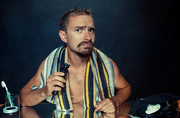 Image showing young man in bedroom sitting in front of the mirror scratching his beard