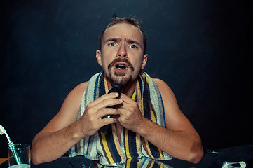 Image showing young man in bedroom sitting in front of the mirror scratching his beard