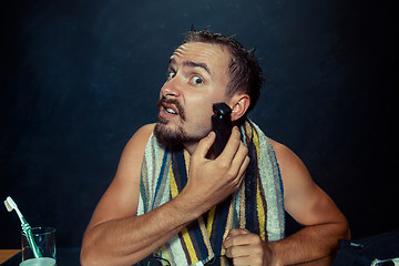 Image showing young man in bedroom sitting in front of the mirror scratching his beard