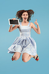 Image showing Image of young woman over blue background using laptop computer or tablet gadget while jumping.