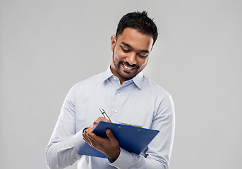 Image showing smiling indian businessman writing to clipboard