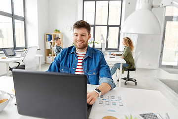 Image showing smiling creative man with laptop working at office