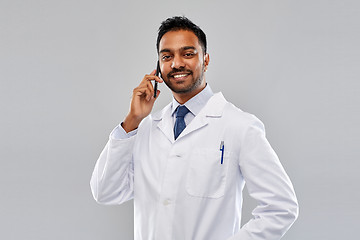 Image showing smiling indian male doctor calling on smartphone