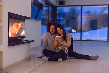 Image showing happy multiethnic couple sitting in front of fireplace