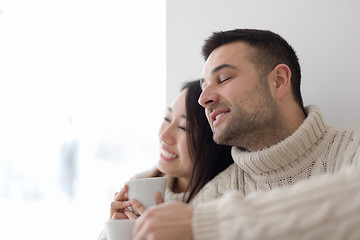 Image showing multiethnic couple enjoying morning coffee by the window