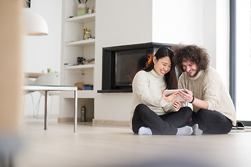 Image showing multiethnic couple using tablet computer in front of fireplace