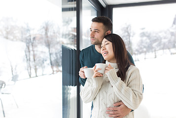 Image showing multiethnic couple enjoying morning coffee by the window