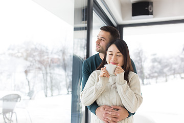 Image showing multiethnic couple enjoying morning coffee by the window