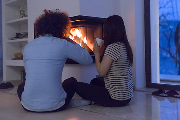 Image showing happy multiethnic couple sitting in front of fireplace