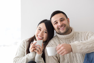 Image showing multiethnic couple enjoying morning coffee by the window