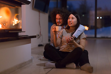 Image showing happy multiethnic couple sitting in front of fireplace