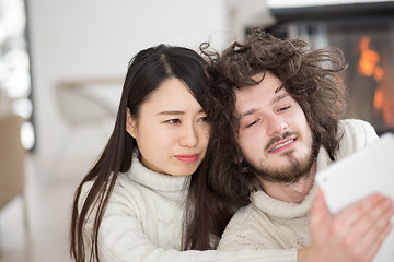 Image showing multiethnic couple using tablet computer in front of fireplace