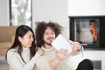 Image showing multiethnic couple using tablet computer in front of fireplace