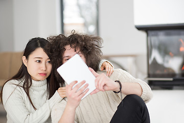 Image showing multiethnic couple using tablet computer in front of fireplace