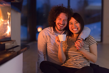 Image showing happy multiethnic couple sitting in front of fireplace