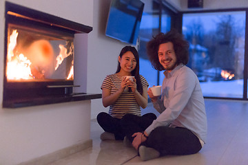 Image showing happy multiethnic couple sitting in front of fireplace