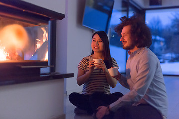 Image showing happy multiethnic couple sitting in front of fireplace