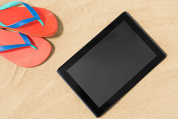 Image showing tablet computer and flip flops on beach sand