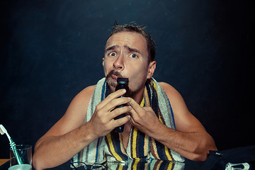 Image showing young man in bedroom sitting in front of the mirror scratching his beard