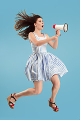 Image showing Beautiful young woman jumping with megaphone isolated over blue background