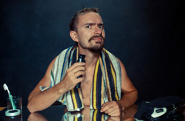 Image showing young man in bedroom sitting in front of the mirror scratching his beard