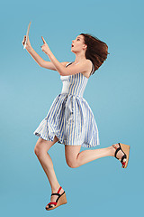 Image showing Image of young woman over blue background using laptop computer or tablet gadget while jumping.