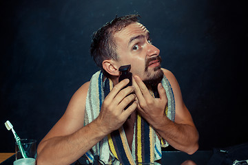 Image showing young man in bedroom sitting in front of the mirror scratching his beard