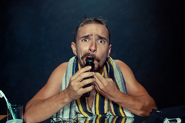 Image showing young man in bedroom sitting in front of the mirror scratching his beard