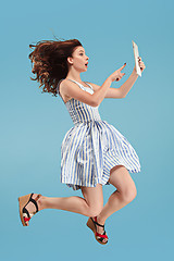 Image showing Image of young woman over blue background using laptop computer or tablet gadget while jumping.