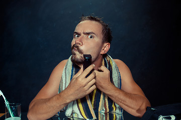 Image showing young man in bedroom sitting in front of the mirror scratching his beard