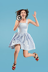 Image showing Beautiful young woman jumping with megaphone isolated over blue background