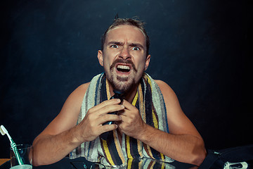 Image showing young man in bedroom sitting in front of the mirror scratching his beard