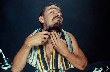 Image showing young man in bedroom sitting in front of the mirror scratching his beard