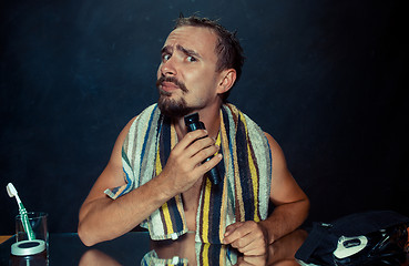 Image showing young man in bedroom sitting in front of the mirror scratching his beard