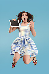 Image showing Image of young woman over blue background using laptop computer or tablet gadget while jumping.