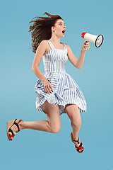 Image showing Beautiful young woman jumping with megaphone isolated over blue background