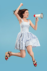 Image showing Beautiful young woman jumping with megaphone isolated over blue background