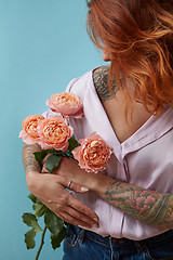 Image showing A girl with a tattoo on her hand holds delicate pink roses around a blue background with space for text. Valentine\'s Day Gift